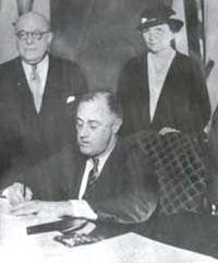 Francis Perkins looks on as Franklin Roosevelt signs the National Labor Relations Act.